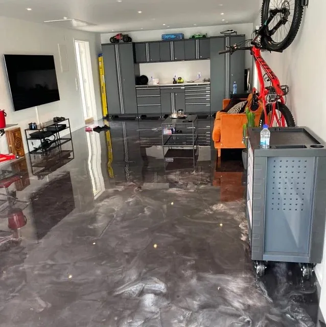 Garasje med sort marmorert epoxygulv, verktøyskap, oransje sofa og sykkel hengt på vegg.