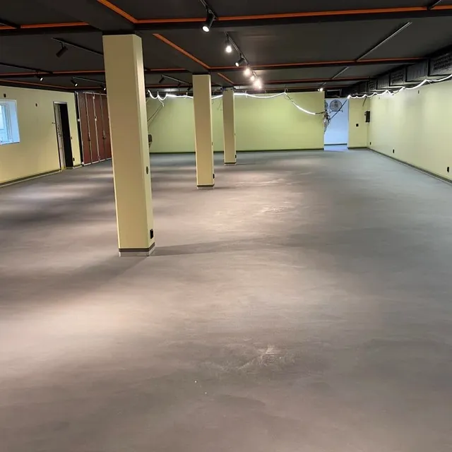 Romslig kjeller eller næringslokale med grått betonggulv og lysegule vegger.