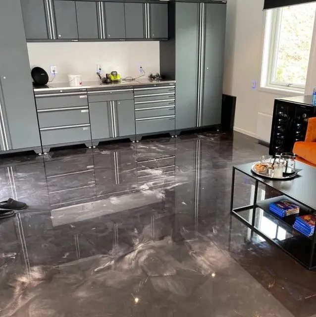 Nærbilde av sort og hvitt marmorert epoxygulv i garasje med grå verktøyskap og arbeidsbenk.