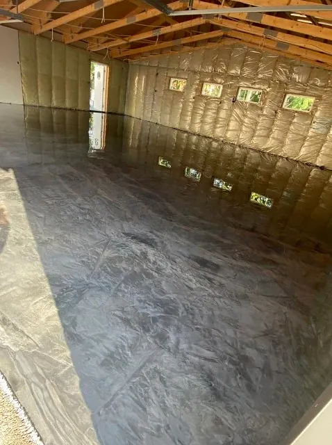 Lagerhall med blankt mørkt epoxybelegg og synlige takbjelker i tre.